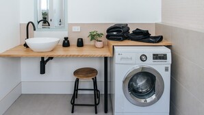 A compact bathroom with a white sink, black faucet, wooden countertop, and a washing machine. - Studio On Lewis Luxury Tiny House 4 mins to town (Mudgee)