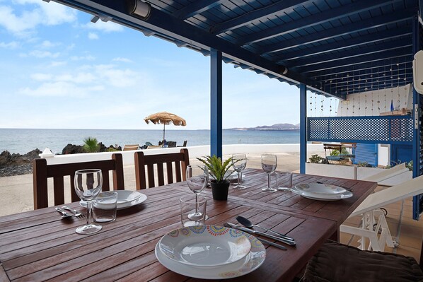 A wooden table set for dining with a view of the sea and a covered area with a blue roof.
