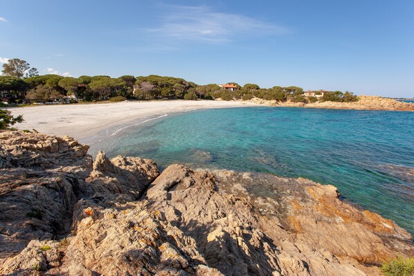 Un paysage côtier caractérisé par un terrain rocheux, des eaux turquoise et limpides, et une plage de sable.