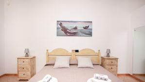 Une chambre à coucher comprenant un lit, deux tables de chevet, une commode, un tableau accroché au mur et une porte.