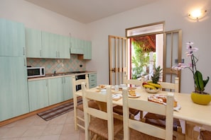 Une cuisine de taille réduite avec des meubles de couleur vert clair, un four à micro-ondes et une table à manger accompagnée de chaises.
