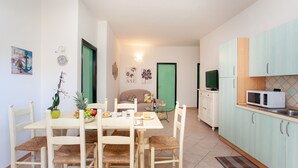 Un coin repas avec une table et des chaises, une cuisine équipée de placards et d’un four à micro-ondes, et une porte verte en arrière-plan.