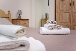 Ein ordentlich gemachtes Bett mit aufgerollten Handtüchern und einem hölzernen Kopfteil.