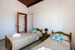 A room with two beds, a wooden door, a nightstand with a lamp, and a tiled floor.