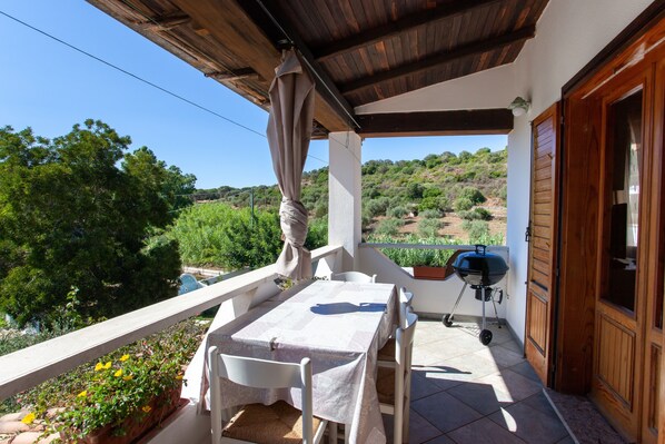 A balcony with a table and chairs, a grill, and a view of the countryside.