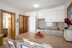 A modern kitchen with white cabinets, a refrigerator, a microwave, and a bowl of fruit on the counter.