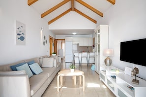 A modern living room with a sofa, a coffee table, a TV, and a kitchen in the background.