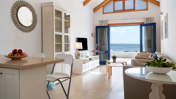 Una habitació amb zona de menjador, sofà, televisió i vistes al mar.