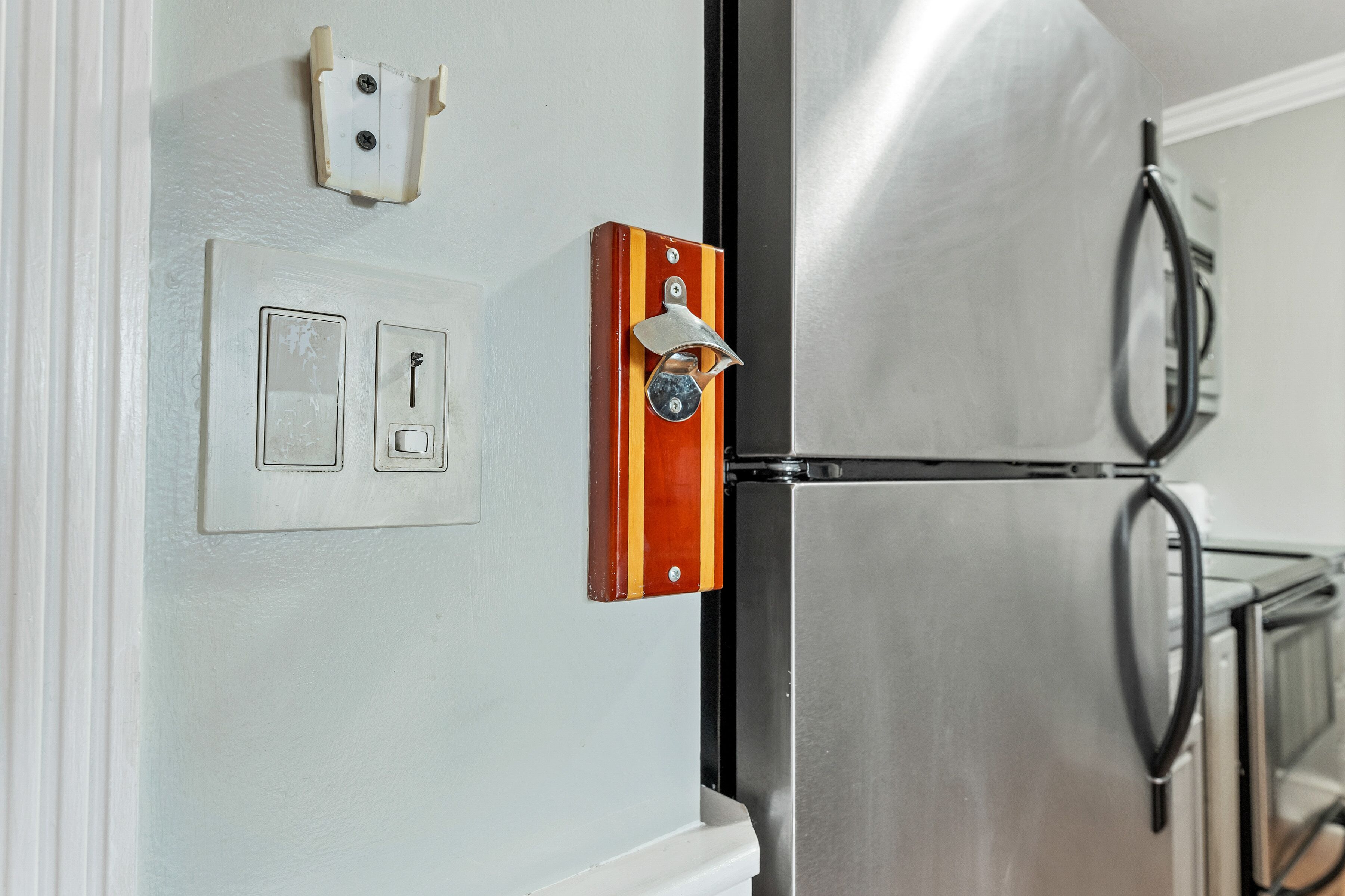 Eine Küche mit einem Edelstahlkühlschrank, einem Holzgriffen und einem an der Wand montierten Lichtschalter.