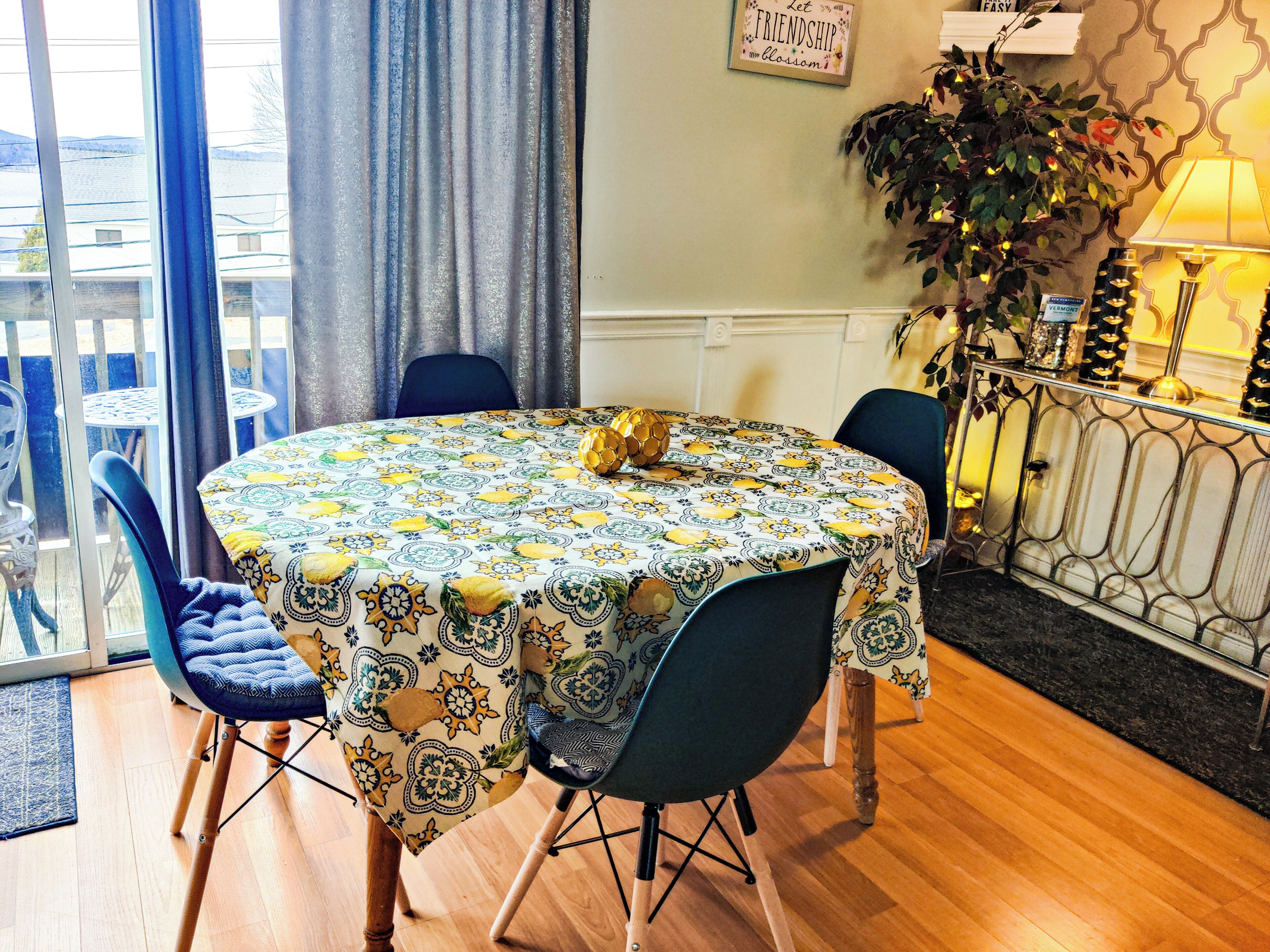 A round table with a patterned tablecloth, surrounded by chairs, in a room with a balcony view.