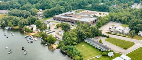 An aerial view of a large industrial building with a parking lot, adjacent to a river with boats docked.