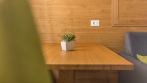 Una mesa de madera con una planta en maceta, un sofá gris con un cojín verde y una pared de madera con un interruptor.