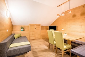 A cozy room with a wooden ceiling, a sofa, a dining table with chairs, and a TV.