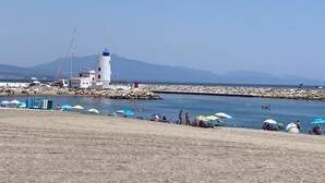 Paesaggio costiero con un faro, un molo roccioso e bagnanti.