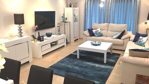 Un soggiorno moderno con TV a schermo piatto, mobile TV bianco, divano color beige e tappeto blu.