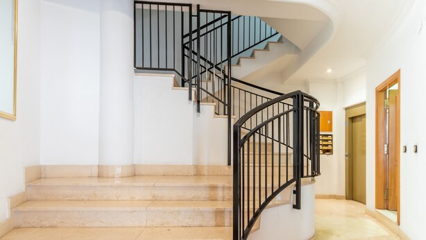 A spiral staircase with black railings, beige marble steps, and a white wall. - Holiday Apartment in Alicante with Air Conditioning & WiFi (Alicante)