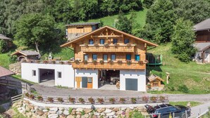 Un edificio de estilo chalet con fachada de madera, balcones con jardineras y un muro de contención de piedra.