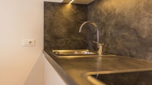 Eine moderne Küche mit Spüle aus Edelstahl, Wandleuchte und einer strukturierten Rückwand.