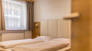 Ein Hotelzimmer mit zwei Betten, einem hölzernen Kopfteil, einem Fenster mit Vorhängen und einer Wandleuchte.