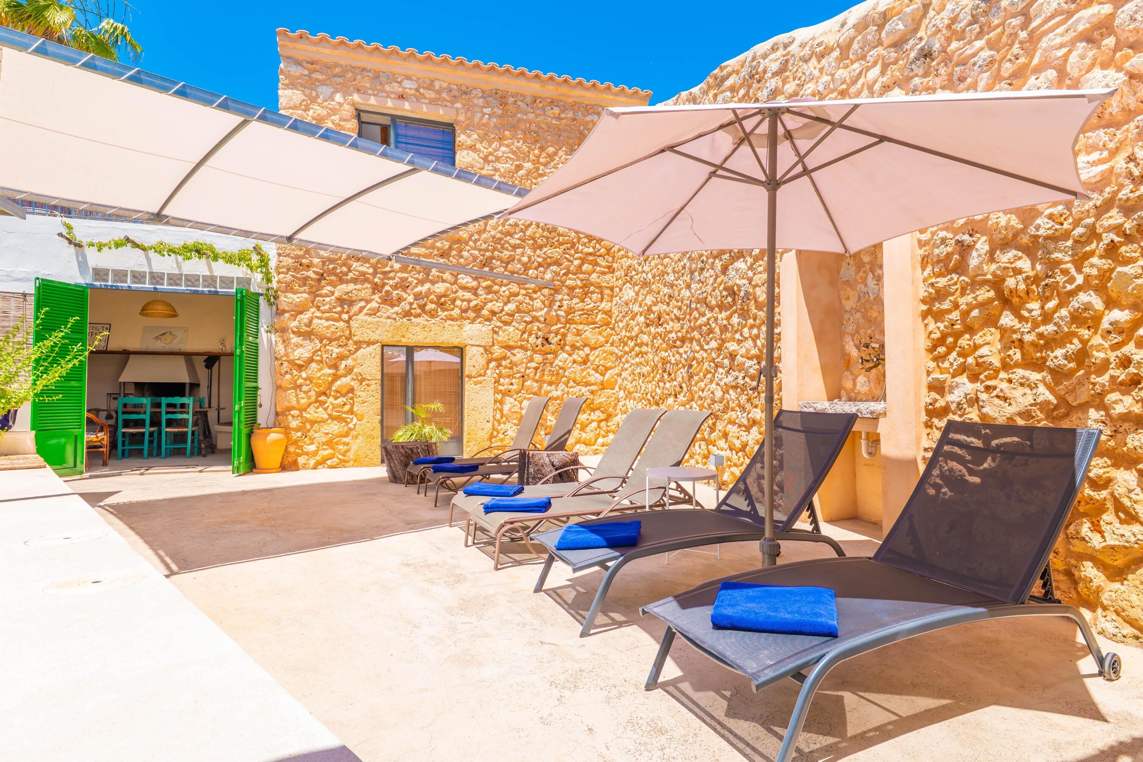 Un bâtiment en pierre doté d’un patio aménagé avec des chaises longues et des parasols.
