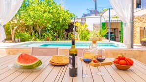 Ett bord vid poolkanten med en flaska vin, ett glas rött vin, en bit vattenmelon, en tallrik med bröd, en skål med tomater och ett glas vitt vin.