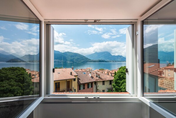 Una habitación con un ventanal que ofrece vistas a un lago, montañas y un pueblo con tejados rojos.