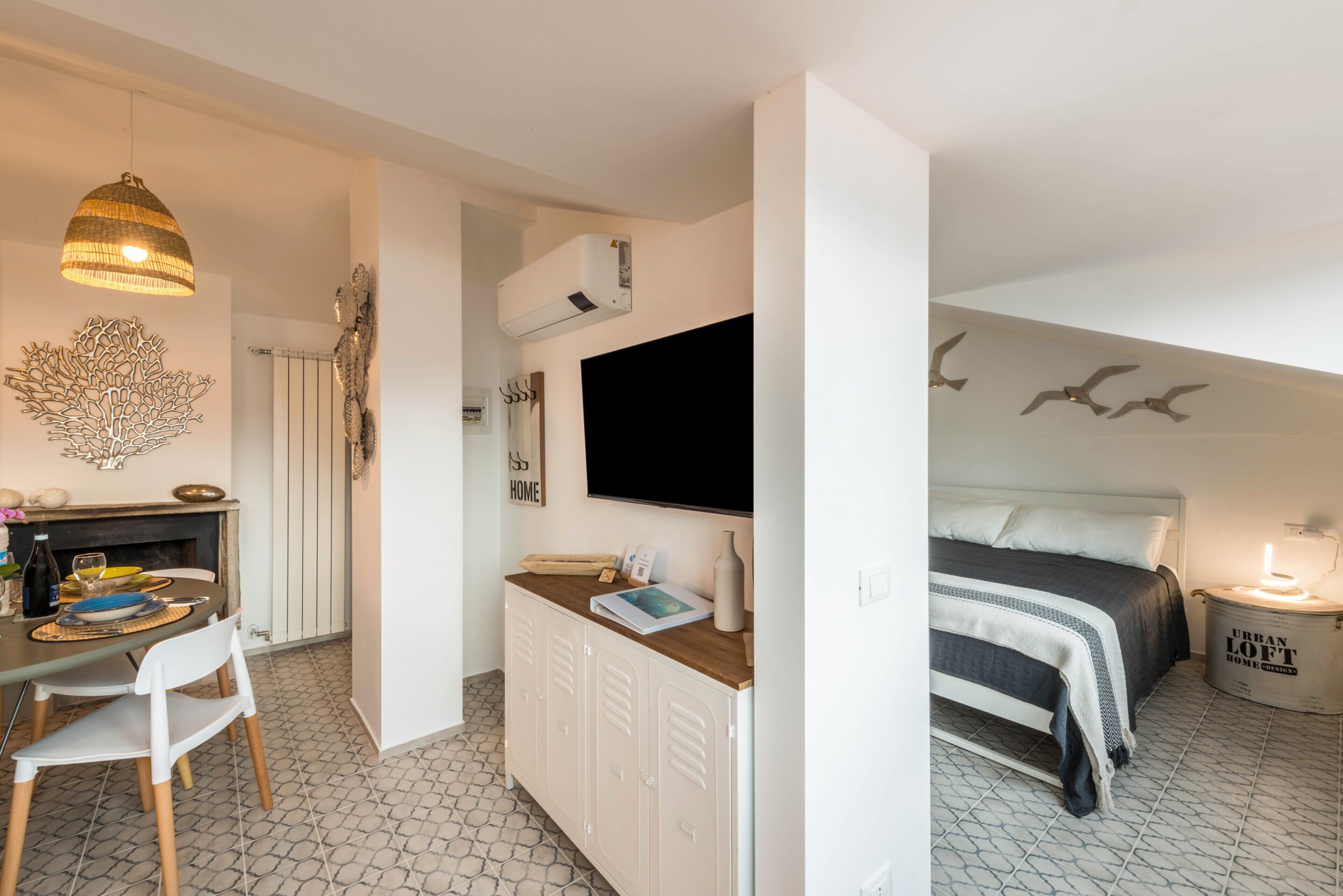 A compact room with a bed, a desk with a chair, a television, and a wall-mounted air conditioner.