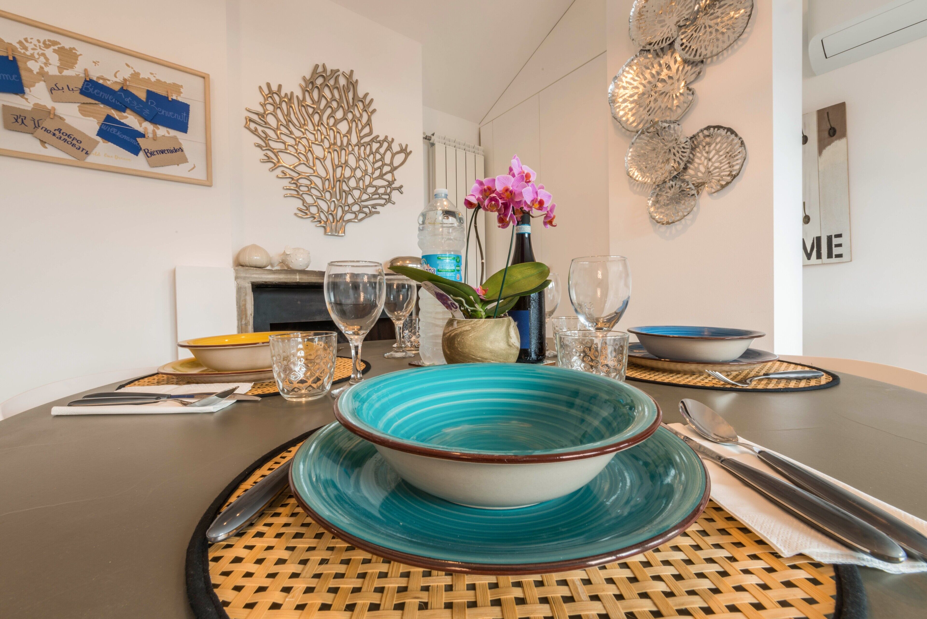 Een eettafel met een blauw-witte schaal, een vaas met roze bloemen en diverse glazen.