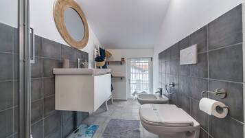 Un baño moderno con ducha, inodoro y lavamanos, con azulejos grises y un espejo con marco de madera.