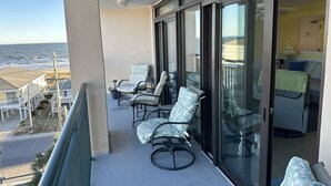 Un balcón con mobiliario exterior, una puerta de cristal que da a una habitación y vista a la playa.
