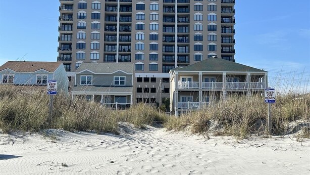 Un hotel de varios pisos con balcones, situado cerca de una zona de playa de arena.