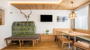 A modern interior with a wooden ceiling, a green mosaic fireplace, a television, and a dining area with wooden furniture. - Holiday Apartment "Runcac Plaies" with Mountain View, Wi-Fi & Balcony (San Vigilio)