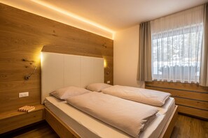 Un lit double avec une tête de lit en bois, des lampes de chevet et une fenêtre ornée de rideaux légers.