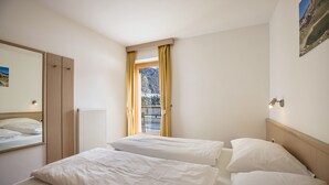 Ett hotellrum med två sängar, ett fönster med gardiner, ett element och en spegel på väggen.