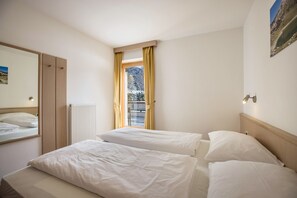 A hotel room with two beds, a window with curtains, a radiator, and a mirror on the wall.