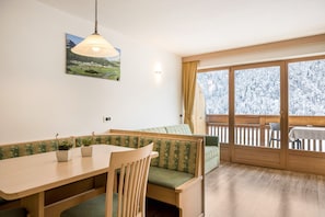 Un espace repas comprenant une table, des chaises, un banc et une vue dégagée sur l’extérieur grâce à une grande fenêtre.