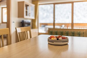 Une table de salle à manger en bois sur laquelle se trouve un panier tressé rempli de fruits.