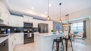 A modern kitchen with white cabinets, stainless steel appliances, and a central island with bar stools.