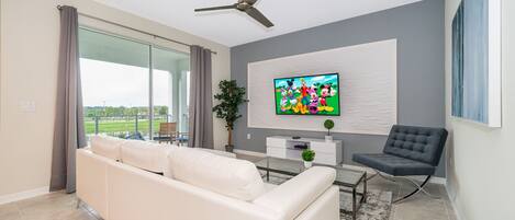 A modern living room with a white sofa, a black chair, a flat-screen TV, and a ceiling fan.