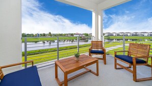 A balcony with wooden furniture, a view of a water body and greenery.