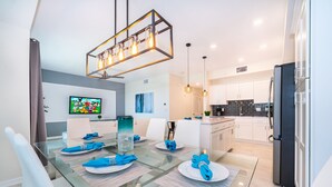 A modern dining area with a glass table, white chairs, and blue napkins.