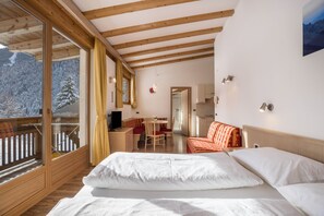 A bedroom with a large bed, wooden beams, a balcony, and a view of snow-covered mountains.