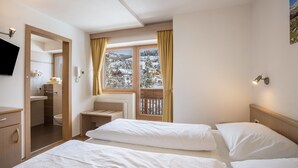 Ein Hotelzimmer mit zwei Betten, einem Badezimmer, einem Fernseher und einem Fenster mit Blick auf eine verschneite Landschaft.