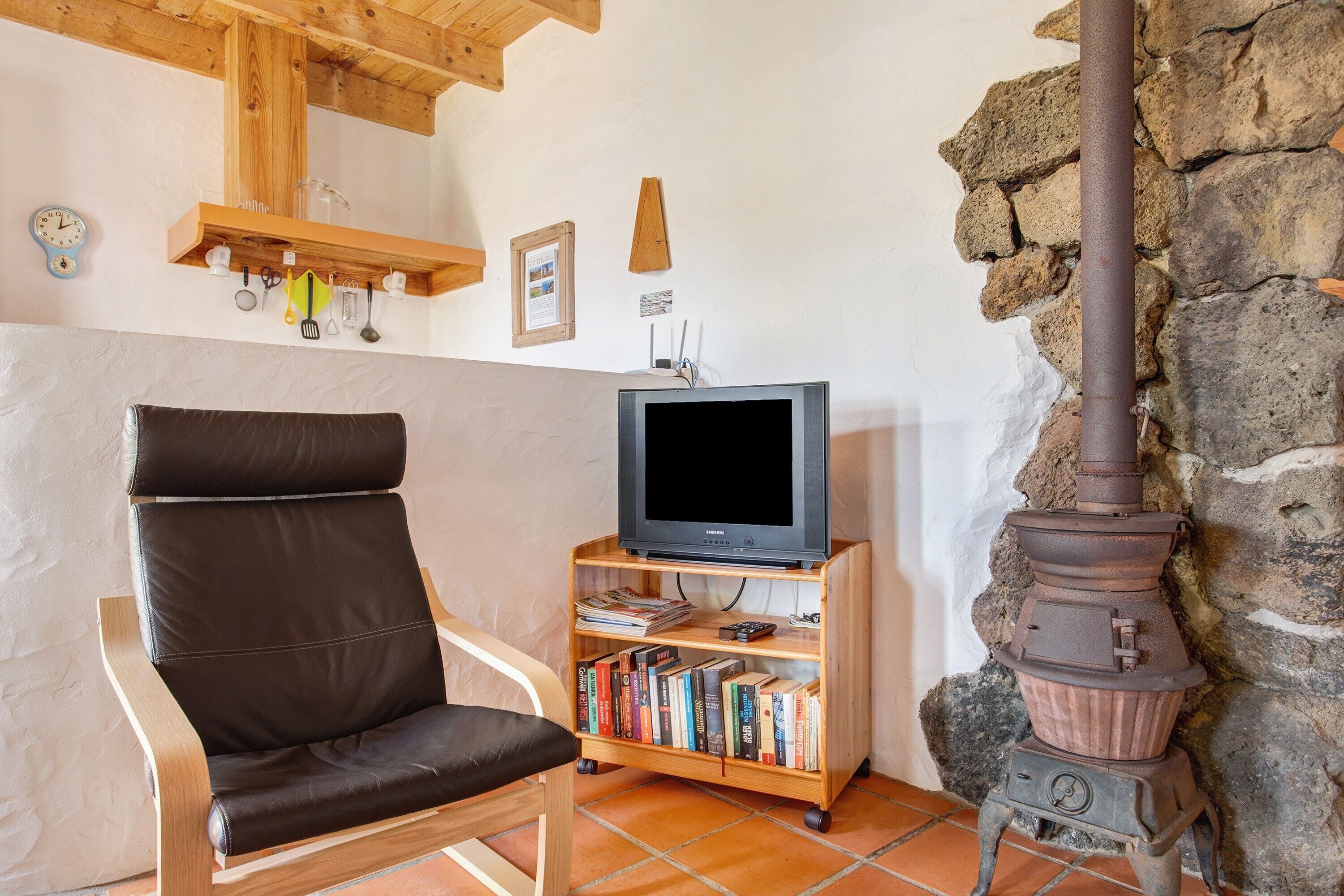 A living room with a wooden chair, a television on a wooden stand, a bookshelf, and a stone wall.