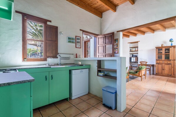 Une cuisine avec des meubles de couleur verte, un lave-vaisselle et une fenêtre donnant sur un paysage verdoyant.