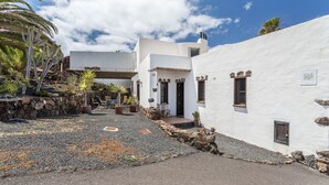 A white building with stone accents, a paved courtyard, and a palm tree. - Holiday Home Casa Cueva with Mountain View, Pool, Wi-Fi & Terrace (Guatiza)