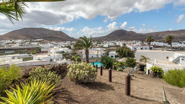 A coastal town with white buildings, palm trees, and mountains in the background. - Holiday Home Casa Cueva with Mountain View, Pool, Wi-Fi & Terrace (Guatiza)
