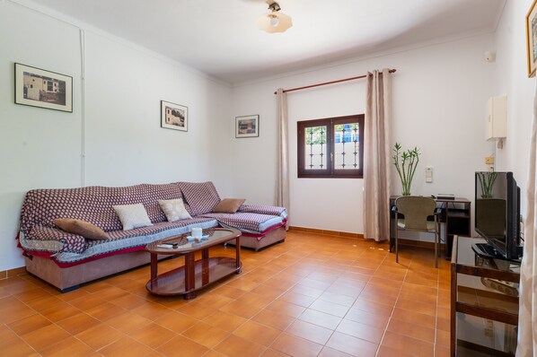 Ein Wohnzimmer mit einer Couch, einem Couchtisch, einem Fernseher und einem Fenster mit Vorhängen.