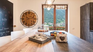 A cozy room with a wooden table, a large round clock, a window with a mountain view, and a chalkboard with handwritten notes.