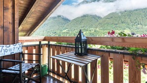 A wooden deck with a view of mountains, a lantern, and a chair.